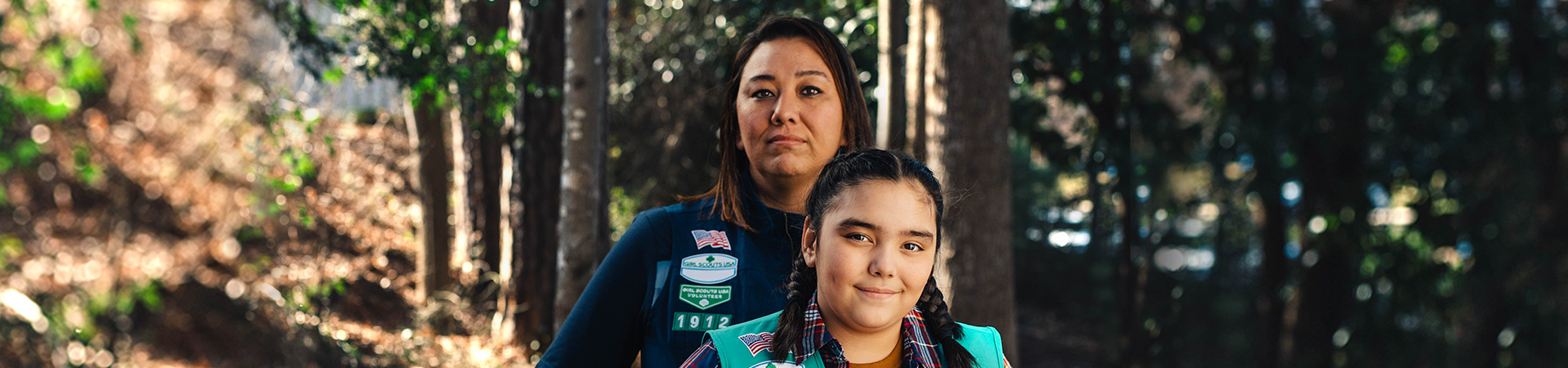  adult woman girl scout volunteer wearing vest outdoors with junior girl scout hiking 