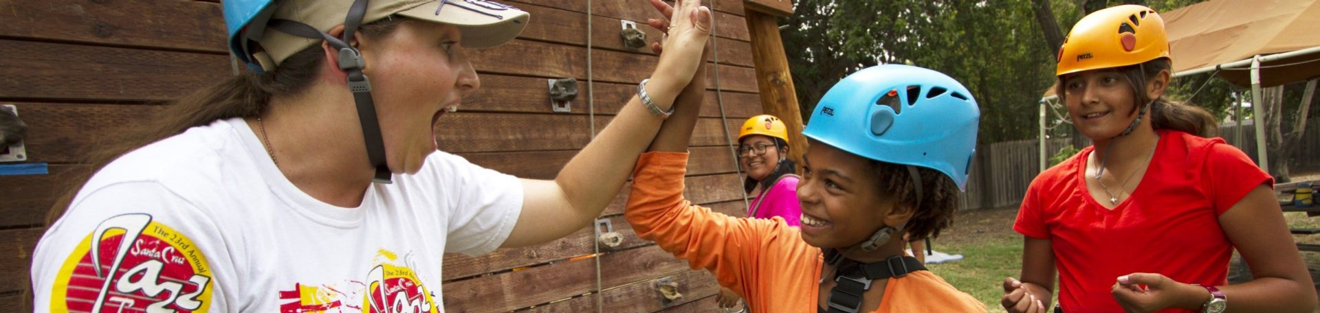  girl scout and volunteer wearing climbing helmets high fiving 