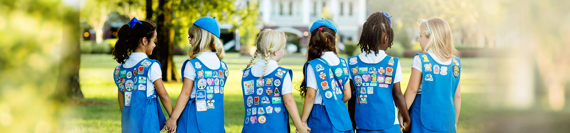  group of daisy girl scouts holding hands in uniform blue apron vest with patches and badges 