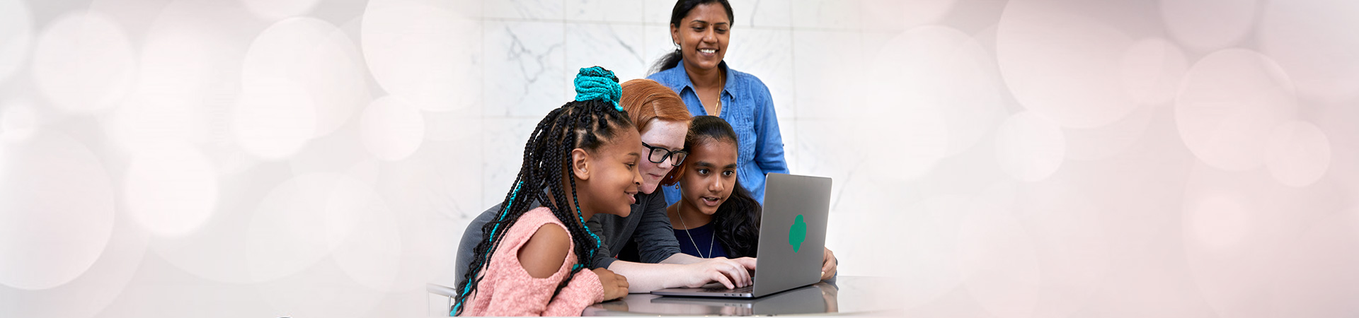  three girls in front of laptop, one mom looking over their shoulder 