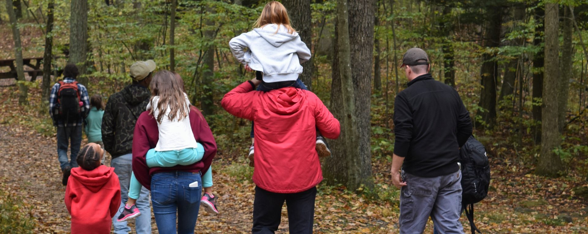  group of people walking in the woods, one young girl on her father's shoulders 