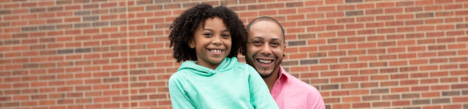  girl and her father smiling standing in front of brick wall 